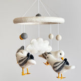 A felt baby mobile featuring four charming seagulls is presented against a light gray wall. Each handcrafted seagull has outstretched wings, with white bodies, gray striped wings, and yellow beaks and feet. The mobile's soft, dreamy aesthetic creates a calming atmosphere, perfect for a nursery.