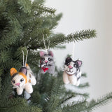 Three charming wool felt cat ornaments, including Calico, Gray Tabby, and Tuxedo designs, hang from a green Christmas tree. The calico cat ornament displays orange and black markings, the gray tabby wears a red bow, and the tuxedo cat has black and white fur. These unique Christmas ornaments are crafted from soft, felted wool with intricate details like whiskers, bright eyes, and a cotton hanging string.