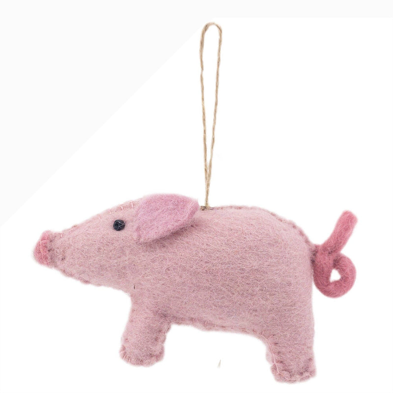 A delightful pink pig felt Christmas ornament, part of the Farmland Animals set, is displayed suspended by a jute string against a bright white backdrop. This handcrafted pig ornament features a rounded body, a curly tail, and small perky ears, all in varying shades of pink. It has a snout and tiny black bead eyes, and its soft wool felt texture adds to its charming, handmade appeal.