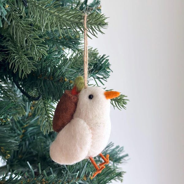 A charming wool felt dove ornament hangs from a green Christmas tree branch. This pure white felt dove features a small black eye, an orange beak, and orange felt feet perched on a needle. A jute string is attached for hanging, as the dove gracefully carries a delicate olive twig.