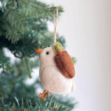 A handcrafted wool felt dove ornament hangs gracefully from a green Christmas tree branch, adding a warm and inviting atmosphere. This Christmas tree ornament features a pristine white body, an orange beak and feet, and delicately holds an olive twig, symbolizing peace.