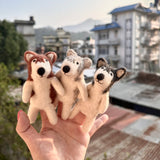 An Alaskan husky dog felt finger puppet is held up by a female hand with red nail polish against a bright, urban backdrop. This unique wool felt finger puppet is meticulously crafted with intricate needle felt detailing, featuring a black nose and upright, triangular ears, showcasing excellent craftsmanship.