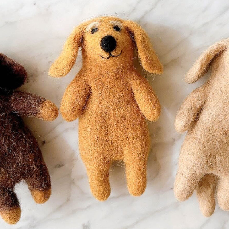 Three handmade felt Dachshund dog finger puppets are displayed on a white surface against a bright, neutral background. These unique finger puppets come in beige, khaki, and brown. Each captures the breed's elongated body and distinctive characteristics, including a black nose and floppy ears.