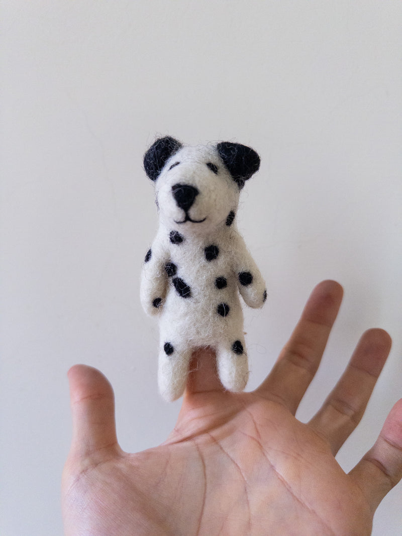 A handmade felt Dalmatian dog finger puppet is presented by a hand against a plain white backdrop. This charming felt finger puppet features a white body with distinct black spots, black ears, and a black nose, showcasing its meticulous handcrafted design.