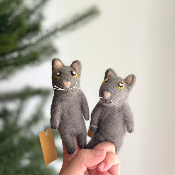 The gray cat felt finger puppet is held in a person's hand against a soft, bright backdrop. This handcrafted felt finger puppet features a gray body with bright yellow eyes, offering a charming felt toy for kids.