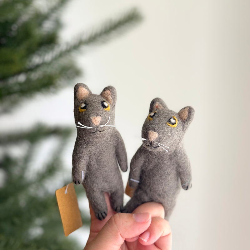 The gray cat felt finger puppet is held in a person's hand against a soft, bright backdrop. This handcrafted felt finger puppet features a gray body with bright yellow eyes, offering a charming felt toy for kids.