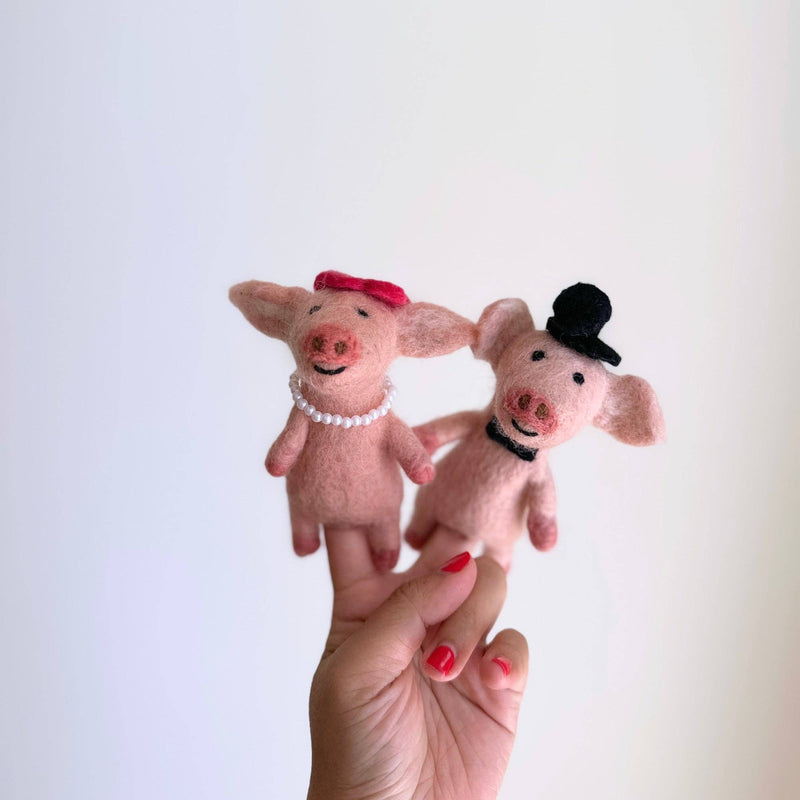 A female hand presents two charming handmade felt duck finger puppets, styled as a couple in honeymoon attire, against a bright background. One felt duck puppet wears a red bow and pearl necklace, while the other sports a black top hat and bow tie. Both feature stitched mouths and button eyes.