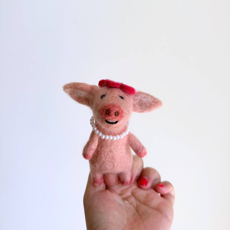 This handcrafted, fair-trade light pink wool felt duck finger puppet is prominently displayed against a bright white background. It wears a bright red hat and a pearl necklace, adding to its whimsical honeymoon attire. Its soft, slightly fuzzy texture highlights its artisanal craftsmanship.