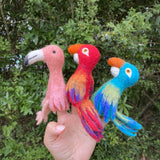 A hand holds three felt finger puppets against a natural background, featuring a parrot, seagull, and elephant. The wool felt puppets have vibrant colors and detailed patterns that mimic the appearance of real birds and an elephant.