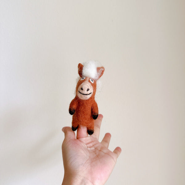 A brown felt horse finger puppet, from a handmade farm animal finger puppet set, stands upright against a plain white background. This charming wool felt horse features a white mane, a stitched smile, and dark hooves, highlighting its delightful craftsmanship.