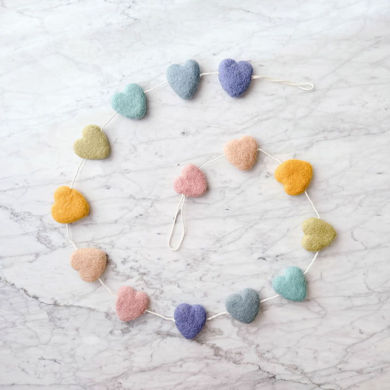 A cheerful felt star garland is artfully arranged in a circular shape on a marbled surface. It features seven pastel rainbow-hued felt stars in shades of blue, purple, pink, yellow, and green. The stars are evenly spaced along a white cotton string, creating a symmetrical and decorative design.