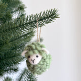 A pastel green felt mini fluffy sheep ornament hangs gracefully from a Christmas tree branch against a plain white background. This handmade felted wool sheep ornament features a textured pastel green body, small white ears, and a white felt face with simple black eyes and a stitched 'Y' mouth. A jute string loop is attached for hanging.