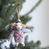 A handcrafted wool felt mouse Christmas ornament hangs from a green Christmas tree branch. The gray mouse, with white and tan details, wears a gray sweater featuring a red snowflake, a matching scarf, and a hat. Suspended by a rustic twine loop, this unique Christmas ornament adds a charming and festive touch to the holiday decor.