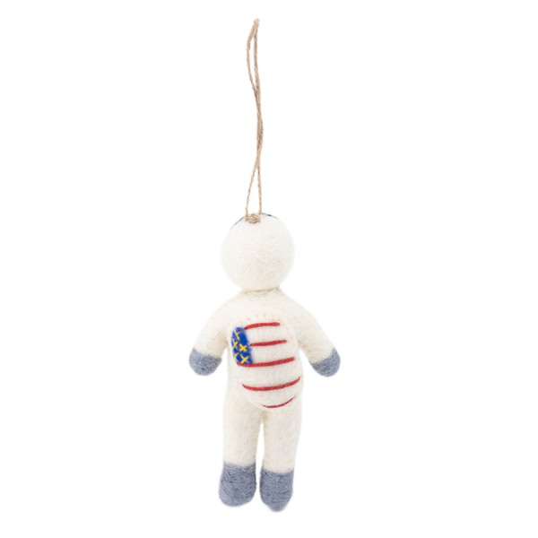 A whimsical felt astronaut ornament floats against a bright white background, suspended by a jute string. This handmade wool felt astronaut has a creamy white body, a spherical head, and soft gray felt tips on its arms and legs. Its chest features a stylized design of blue stars and red stripes, mimicking a flag, adding a sense of childlike wonder.