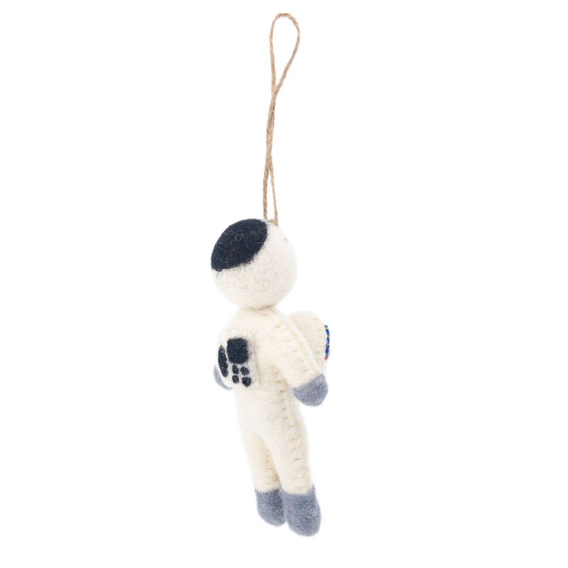 A unique needle felted astronaut ornament, also serving as a keychain, hangs suspended against a stark white backdrop by a knotted jute string. The astronaut wears a creamy white spacesuit detailed with gray gloves and boots. Its helmet is half black, and a flag adorns its chest.