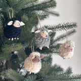 Fluffy sheep felt ornaments are displayed on a Christmas tree. These needle felted sheep ornaments, in black, gray, and white, feature a fluffy, woolly texture with small ears and tiny legs. Each is suspended by a jute string, highlighting them as charming Christmas tree ornaments.