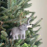 A gray needle felted elephant ornament hangs on a Christmas tree, set against a soft, neutral backdrop. Crafted from textured wool felt, this unique Christmas ornament features a charming raised trunk, small ears, and a fluffy black yarn tail, with a jute string for easy hanging.