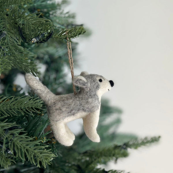 A felt husky ornament hangs on a Christmas tree, adding a whimsical touch. This handmade felt ornament features a mix of gray and white, characteristic of a husky.