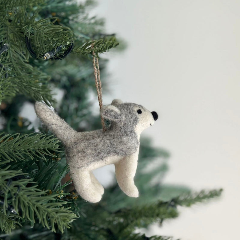 A felt husky ornament hangs on a Christmas tree, adding a whimsical touch. This handmade felt ornament features a mix of gray and white, characteristic of a husky.