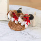 A playful felt Jack Russell dog ornament is showcased on a rustic woven mat, against a bright, airy background. This adorable 3D wool felt Jack Russell dog ornament is expertly crafted in white, brown, and black, featuring small black eyes and a red cotton string around its neck, highlighting its handmade charm.