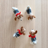 Four unique Jack Russell dog felt ornaments are playfully arranged on a light wooden surface. Each needle felted wool felt ornament, handcrafted from organic materials, features a different pose in white, grey, and brown with distinct brown ears and a red collar. A white cotton string is attached for hanging as a Christmas tree ornament.