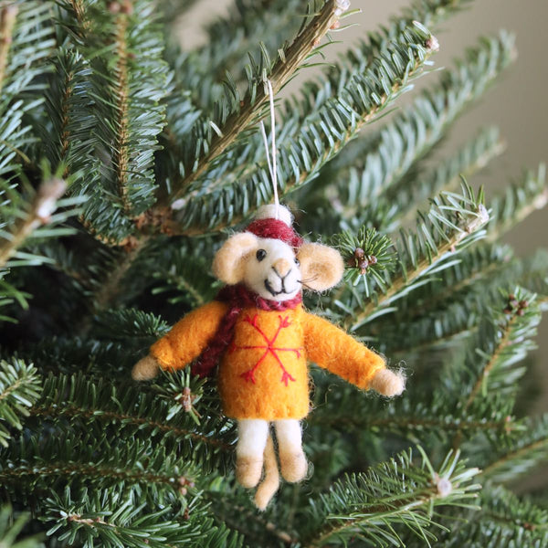 A charming needle felted wool mouse ornament, featuring a red and white hat, red scarf, and yellow sweater, is displayed on a Christmas tree. The yellow sweater is adorned with a red snowflake. The mouse ornament is suspended by a white cotton string.