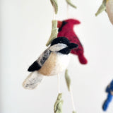 A needle felted chickadee ornament hangs against a plain white background, showcasing its handcrafted detail. This wool felt chickadee features a distinctive black cap and throat, white cheeks, and a tan body. Its round, textured form, suspended by a jute thread, evokes a natural, rustic charm.