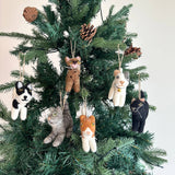Several playful wool felt cat ornaments adorn a Christmas tree with green needles and pine cones, creating a festive scene. Each handcrafted felt cat ornament is meticulously hand-stitched with intricate embroidery, detailing whiskers and expressive faces. These unique Christmas ornaments come in various colors and patterns, including black and white, brown spotted, white with gray, black, gray, and orange and white, some featuring small golden bells and a jute string.