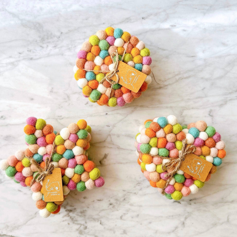 Three handcrafted felt pastel coasters are neatly bundled with a jute string on a white marble surface, highlighting their decorative appeal. Each round, 4-inch coaster is crafted from 100% organic lamb wool, densely arranged with hand-stitched half-inch felt balls in soft pink, orange, green, yellow, blue, and white pastel tones. These unique, ethically handmade wool felt coasters embody a cozy, eco-friendly design, supporting Nepalese female artisans.
