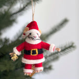 A playful felt Santa Mouse ornament hangs from a Christmas tree branch by a jute string. This handcrafted wool felt ornament features a white-faced mouse with beige ears and long black whiskers. Dressed in a classic red Santa suit, trimmed with white faux fur and cinched by a black belt with a gold buckle, the Santa mouse holds a tiny gold bell.