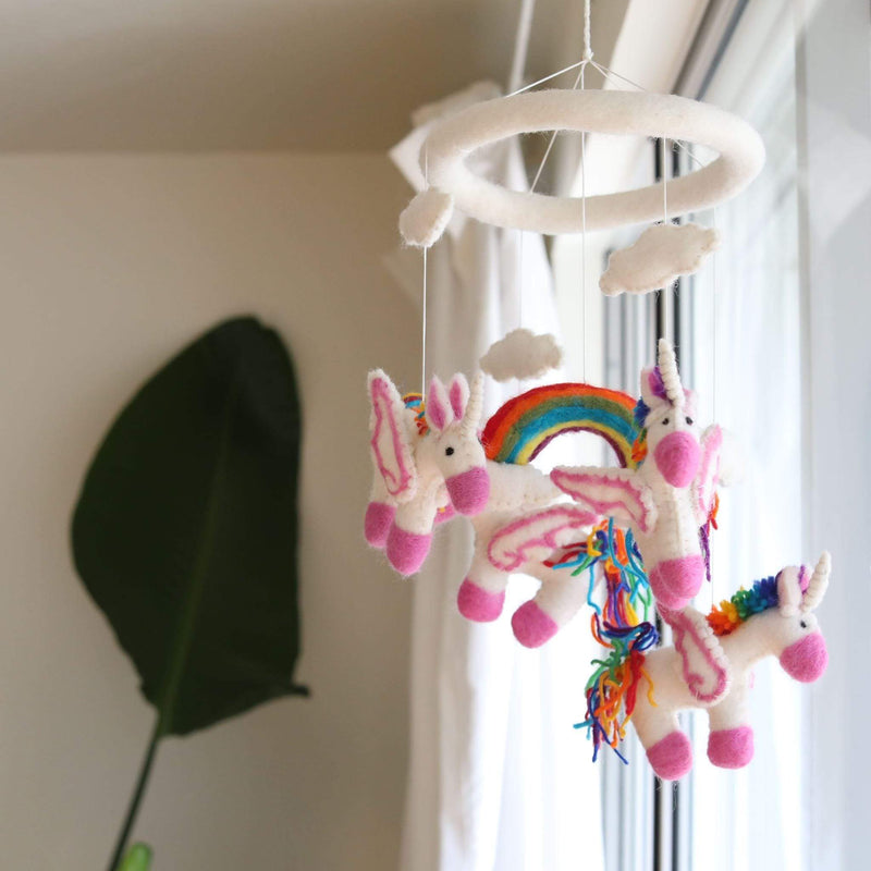 A felt unicorn baby mobile hanging from a ceiling hook, featuring two unicorns with rainbow manes and tails. The room has a calm atmosphere, and the mobile adds a playful touch. Made of 100% New Zealand wool felt, each figure is needle felted individually in 3D design.