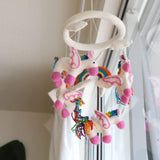 A colorful felt unicorn baby mobile hangs from a ceiling hook, featuring multiple unicorn figures in various poses. Each figure has a unique design with different colors and patterns on their mane and tail.