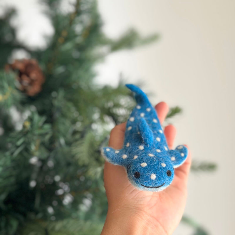 A unique blue felt whale shark finger puppet is held gently in a female hand. This handcrafted felt kids toy features distinctive white markings resembling a starry night sky, tiny black eyes, and a stitched smile.