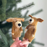 A handmade Golden Retriever wool felt finger puppet is displayed on a female hand, set against a blurred Christmas tree background. Crafted with care, this charming needle-felted Golden Retriever puppet features a black nose, small ears, and white paws. Its intricate details and soft texture capture the lovable expression of the breed, highlighting skilled craftsmanship.