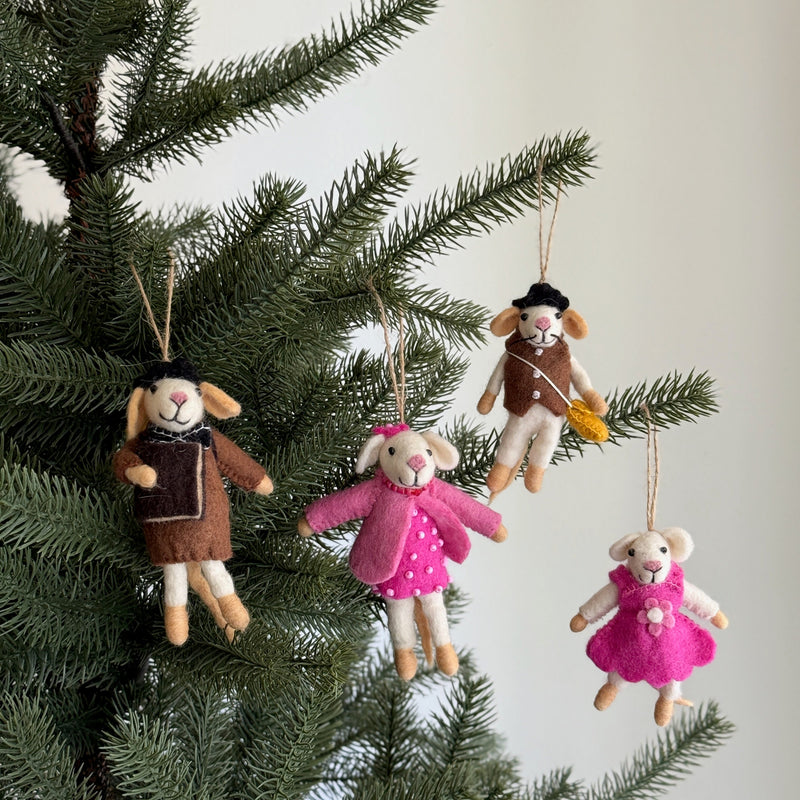 Four festive Felt Mouse Family Ornaments hang from the branches of an evergreen Christmas tree, set against a soft white backdrop. The handcrafted set includes a papa mouse wearing a brown coat and black and white scarf, a mama mouse in a pink coat and dress, a boy mouse with a brown vest, black hat, and yellow satchel, and a girl mouse in a pink dress, bringing a warm, playful touch to the holiday decor.