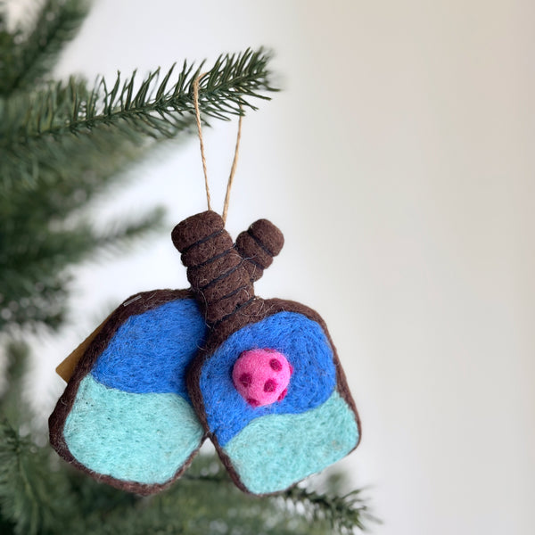 A vibrant wool felt pickleball ornament hangs from a Christmas tree. This handmade ornament is shaped like a pickleball paddle, crafted from wool felt in vibrant colors, and features a jute string for easy hanging.