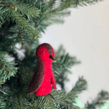 A handmade felt robin finger puppet, a vibrant handcrafted felt kids toy, sits on a Christmas tree branch. This charming, fair-trade felted finger puppet features a bright red body with darker brown head and wing accents, and a black beak. Lovingly crafted from eco-friendly felt, this unique finger puppet brings a touch of nature's magic to playtime.