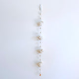 A fluffy felt sheep garland hangs against a stark white wall, featuring three evenly spaced, three-dimensional wool felt sheep. Spherical wooden beads connect the sheep, and a single copper bell hangs at the bottom, creating a serene, neutral-toned display.
