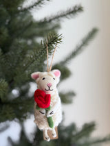 A wool felt sheep ornament holding a heart hangs on a cheerful Christmas tree. This soft, fluffy ornament features tiny pink ears, a pink stitched nose, and closed stitched eyes, with a jute string for hanging.