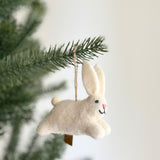 A white bunny ornament is prominently displayed on a vibrant green tree branch, set against a soft white background. This charming handmade felt bunny features long, soft pink ears, a pink nose, black eyes, and a stitched black mouth, suspended by a rustic jute string.
