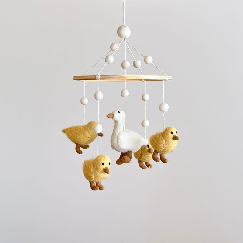 A felt baby mobile, featuring five white call ducks in various poses, hangs from a wooden hanger. The largest duck is at the center, surrounded by smaller ones, against a neutral background.