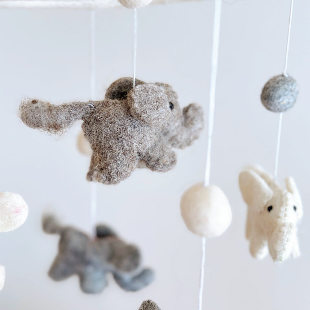 A felt baby mobile, featuring a small elephant figure, hangs from a string in a cozy nursery setting. The mobile's design elements are simple yet charming, with the elephant figure being the central focus. Made from 100% wool felt, this handmade mobile adds a touch of warmth and comfort to any baby's sleeping space.