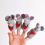 Handcrafted needle felted mouse finger puppets, each holding a heart, are displayed in a female hand against a plain white backdrop. These unique 3D wool felt finger puppets feature gray bodies with pink ears and noses, delicate black whiskers, and a bright red heart.